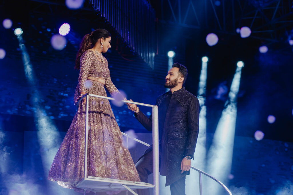 Bride walks an illuminated runway toward the groom during a sangeet performance